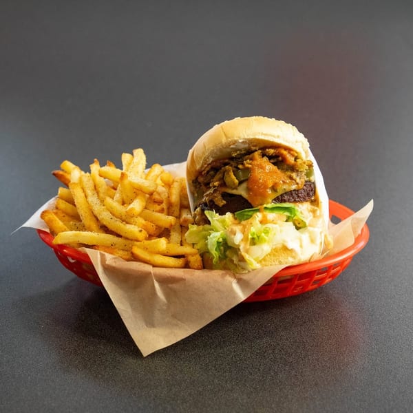 A burger with lettuce, sauce, and toppings, served with a side of french fries in a red basket.