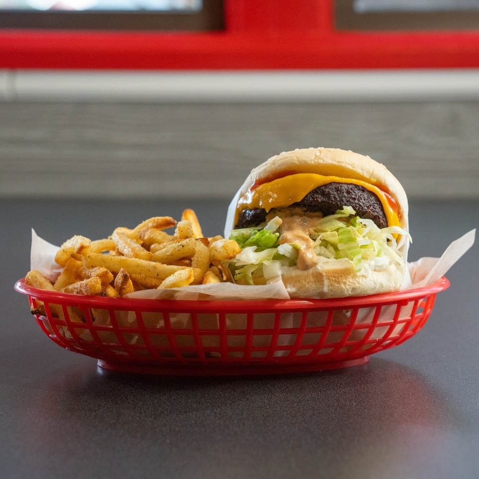 Cheeseburger with lettuce, special sauce, and a side of seasoned fries in a red basket.