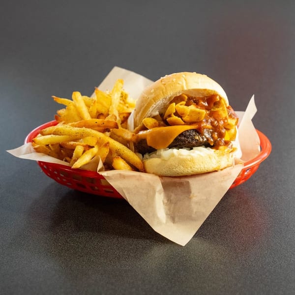 Chili cheeseburger with Fritos and a side of fries in a red basket.