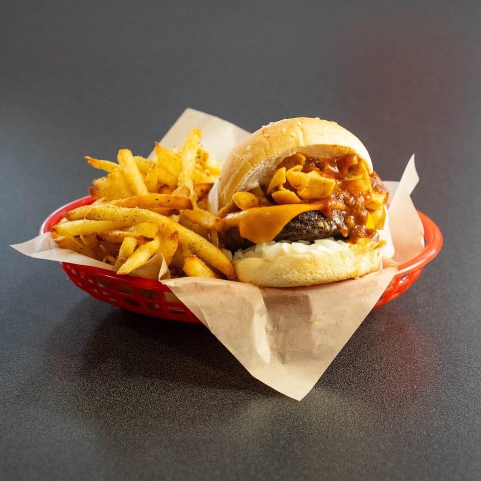 Chili cheeseburger with Fritos and a side of fries in a red basket.