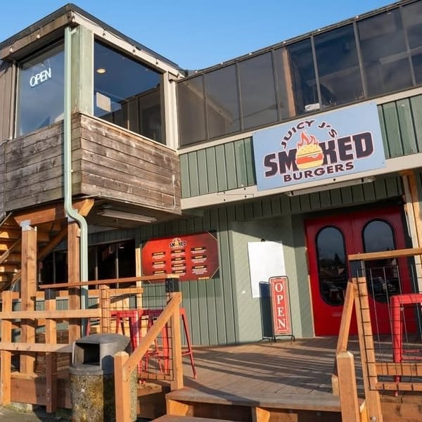 Exterior of Juicy J's Smoked Burgers, a two-story building with wooden stairs and an "Open" sign.