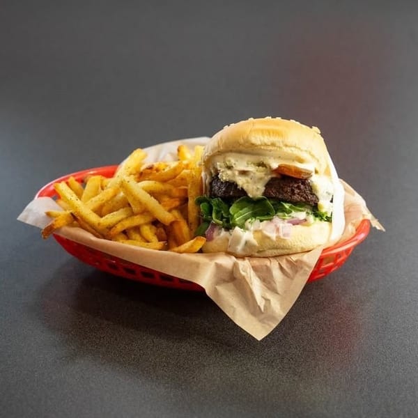 Gourmet burger with fries in a red basket, featuring a thick patty, arugula, and creamy sauce.