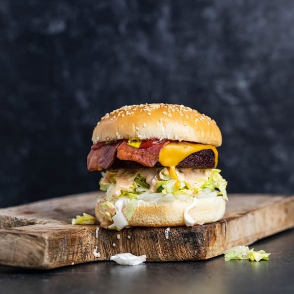 A juicy burger with melted cheese, bacon, lettuce, and sauce on a wooden board.