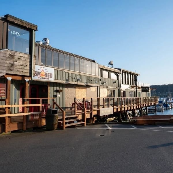 Waterfront restaurant with an "Open" sign, a long wooden deck, and boats docked in the water.